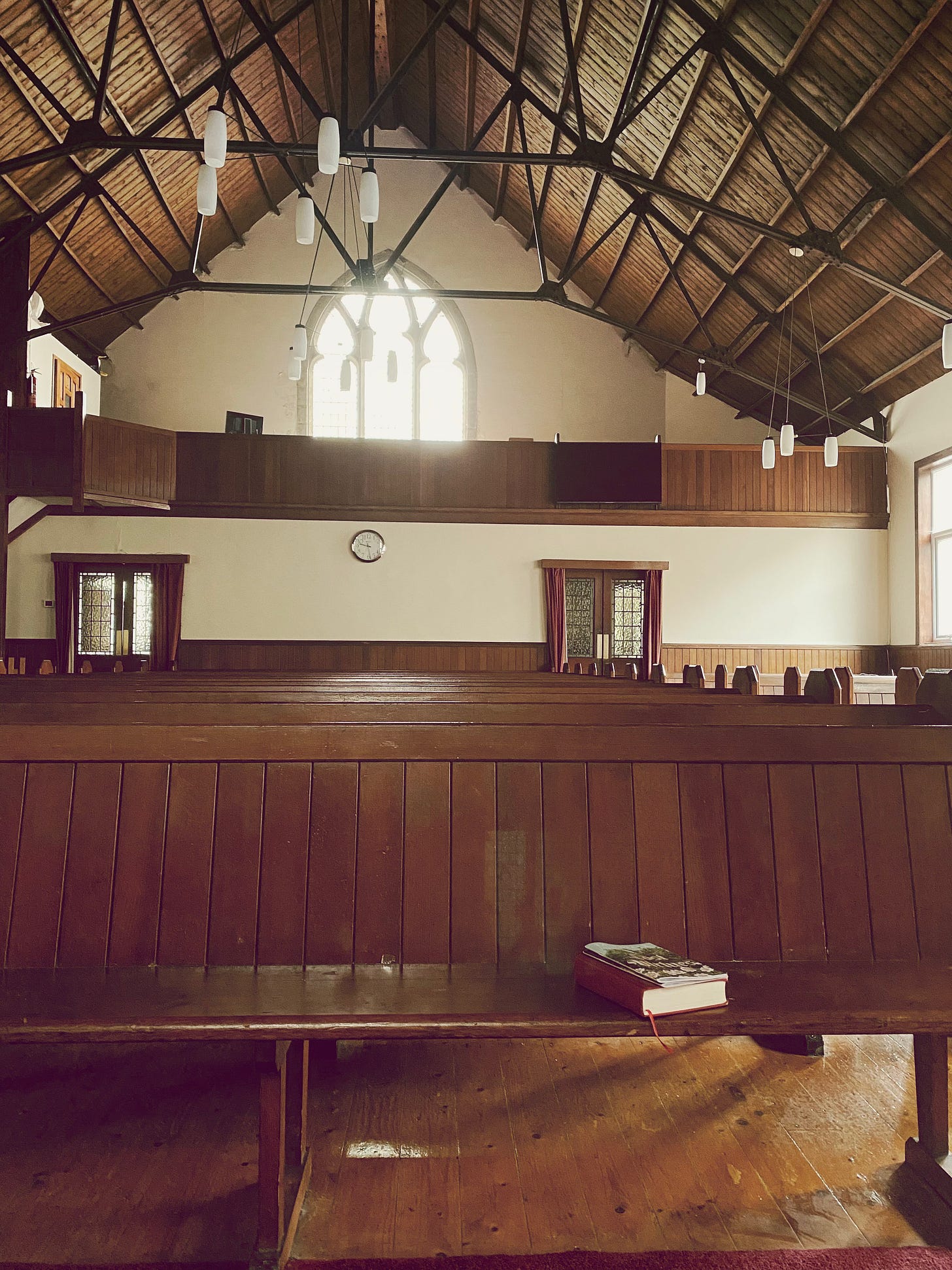 A church sanctuary with pews and light shining in through a stained-glass window.