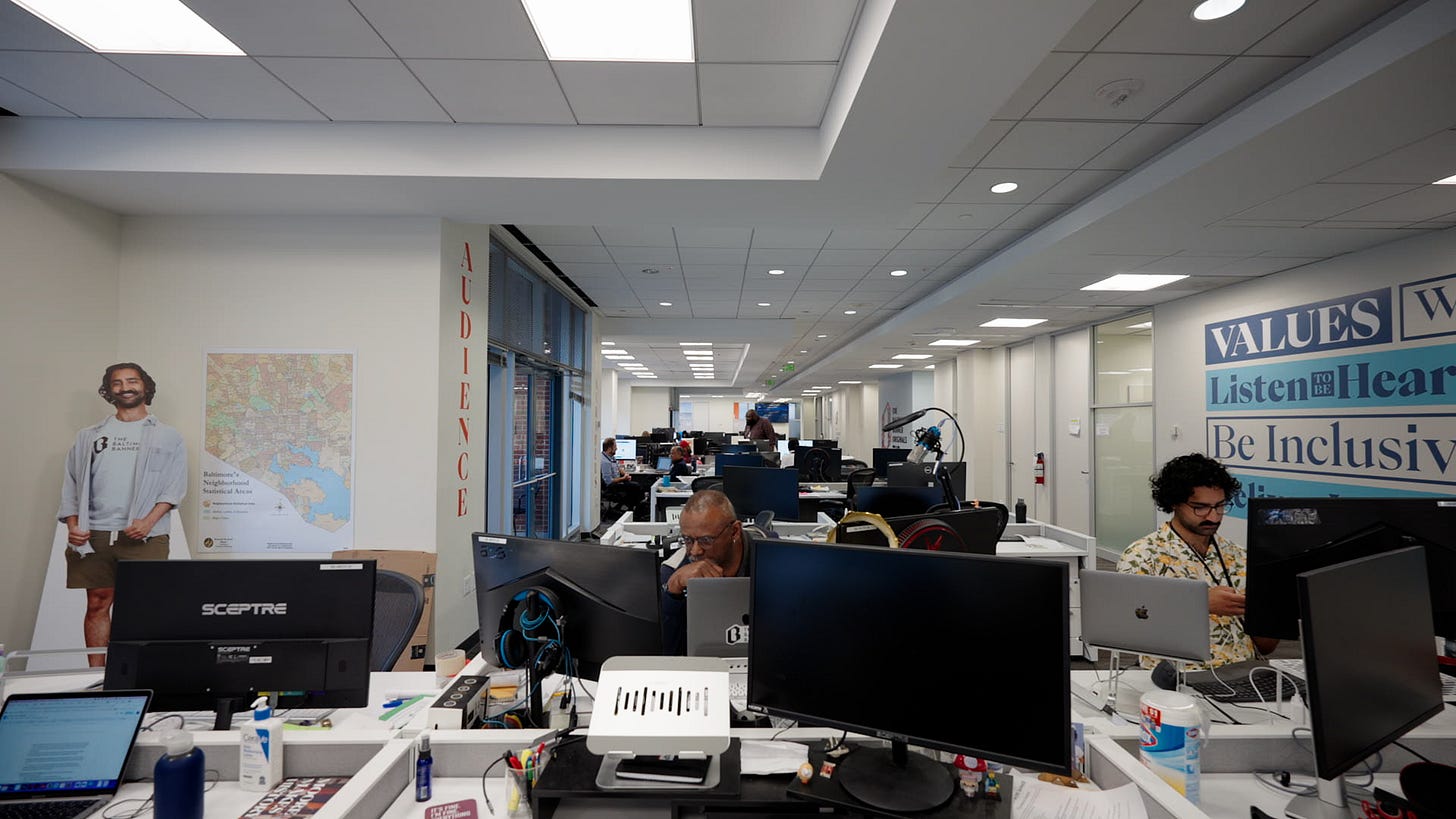 a newsroom with computers and two people sitting at their desks a newsroom with computers and two people sitting at their desks