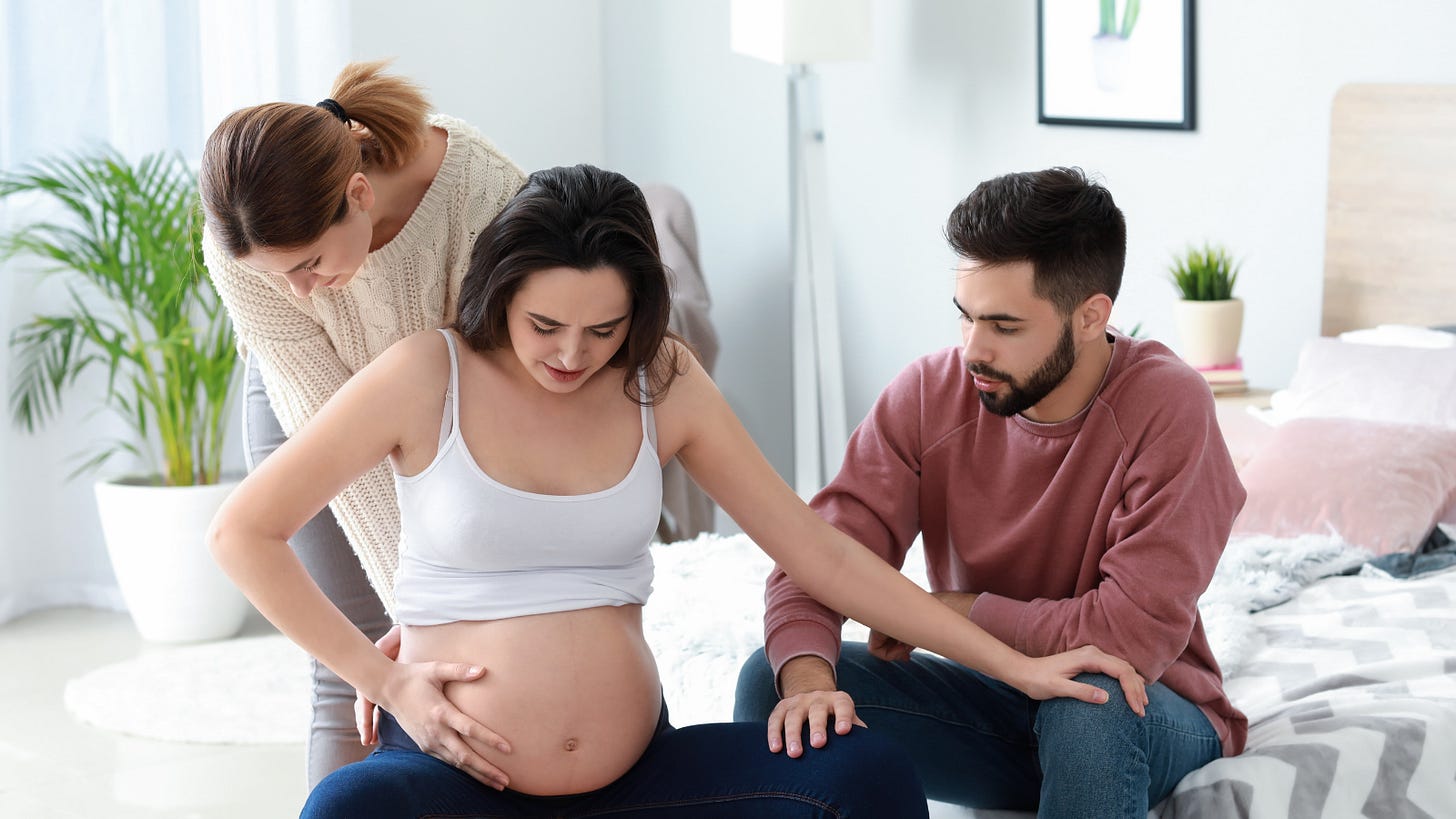 Gestational surrogate during pregnancy with intended parents supporting her as they prepare to welcome their baby.