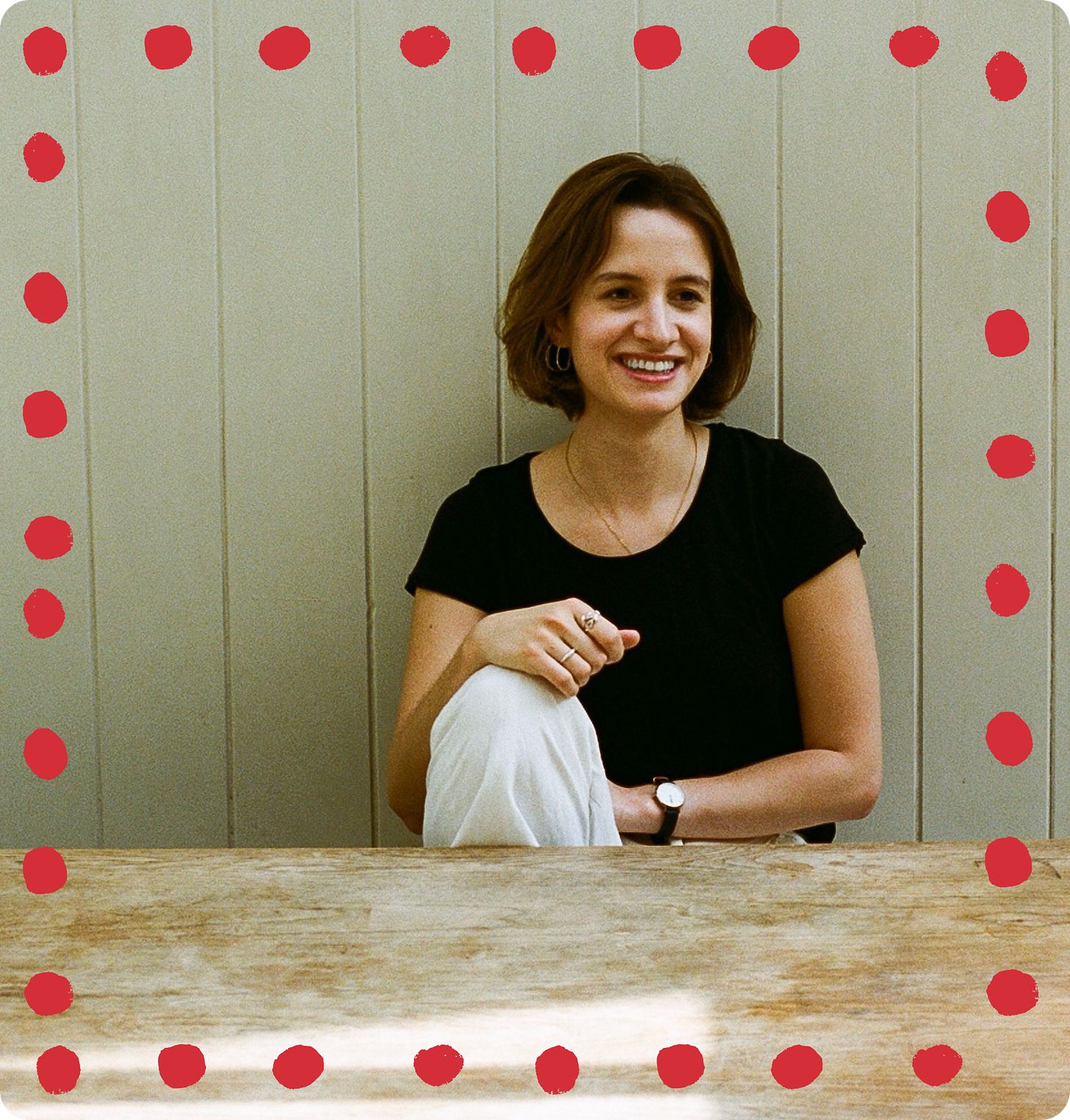 A photo of Celestine, a 30 year old white woman with dark brown hair in a bob. She's wearing a black t-shirt, white trousers, and is sitting at a table with one knee up and one hand on her knee. She looks relaxed and has a wide smile. A photo of Celestine, a 30 year old white woman with dark brown hair in a bob. She's wearing a black t-shirt, white trousers, and is sitting at a table with one knee up and one hand on her knee. She looks relaxed and has a wide smile.