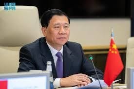 A man in a suit is sitting at a table; a Chinese flag can be seen in the background.