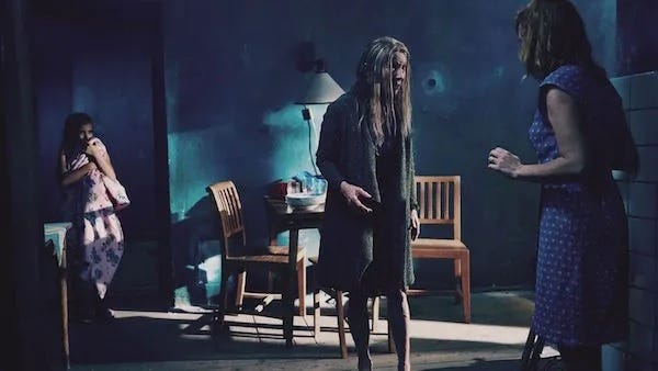 An elderly lady, a little girl and a middle-aged woman stand in a room. The little girl appears scared.