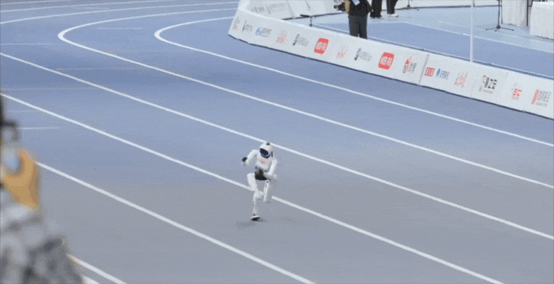 A small white humanoid robot sprinting down marked lanes on a blue indoor running track, then stumbling forward. A small white humanoid robot sprinting down marked lanes on a blue indoor running track, then stumbling forward.