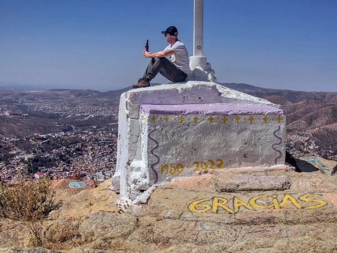 Ian sits beneath the cross at the summit with a bottle of beer