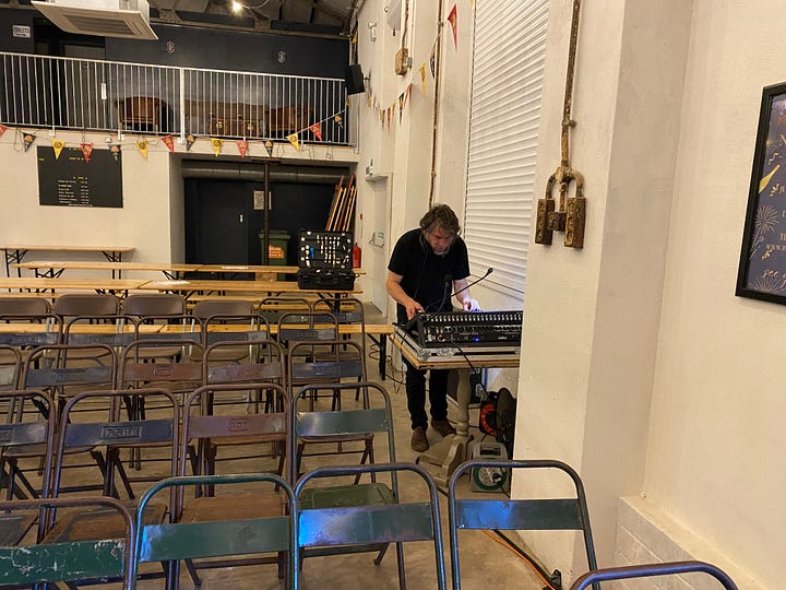 Inside a big warehouse style venue with stage and musical equipment. Stef from Pukka PA Hire setting up