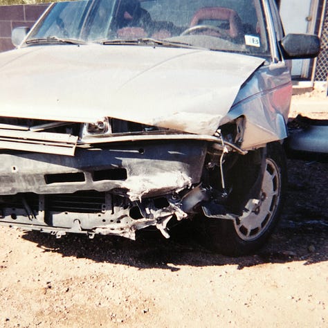 My champagne Mazda 626 lurches cockeyed in the wreck yard with other munched vehicles. The smashed front bumper lies on the ground. The windshield is lanced with cracks. The passenger side is caved in. The drivers side is demolished.