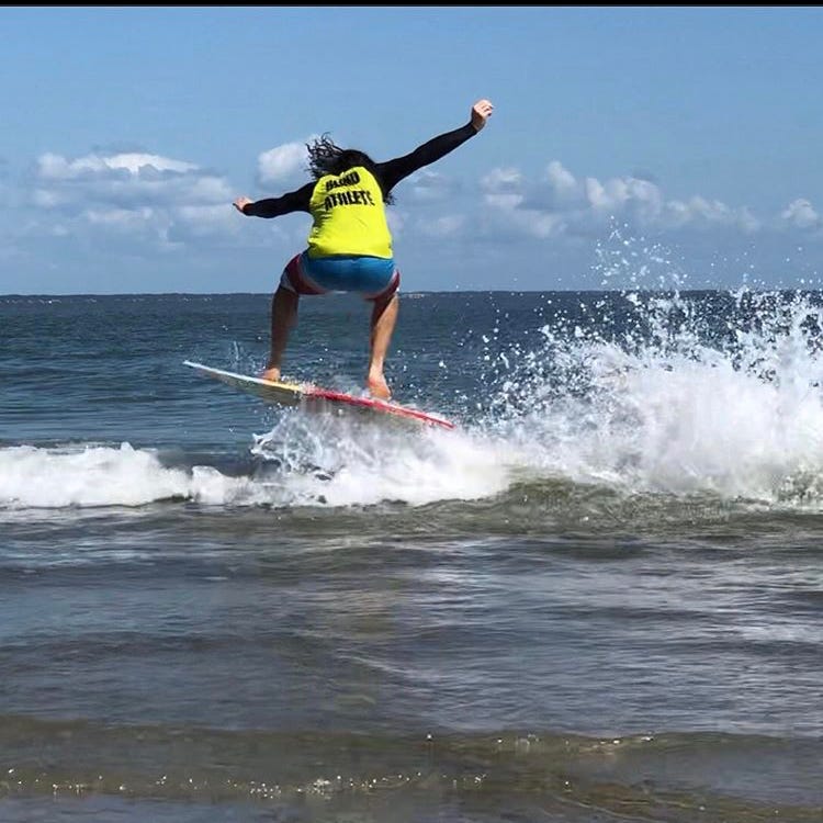 An image of Kai skimboarding and catching air off the waves. He's wearing a jersey which reads "Blind Athlete" across the back. An image of Kai skimboarding and catching air off the waves. He's wearing a jersey which reads "Blind Athlete" across the back.
