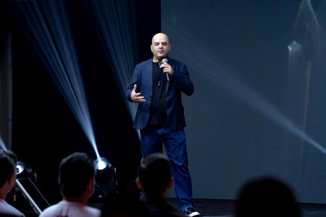 imagem do palestrante de vendas Leandro Branquinho em um palco diante de uma plateia em uma convenção de vendas. O palco tem iluminação parecida com um show de banda imagem do palestrante de vendas Leandro Branquinho em um palco diante de uma plateia em uma convenção de vendas. O palco tem iluminação parecida com um show de banda