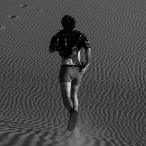 a man walking across a sandy field with footprints in the sand