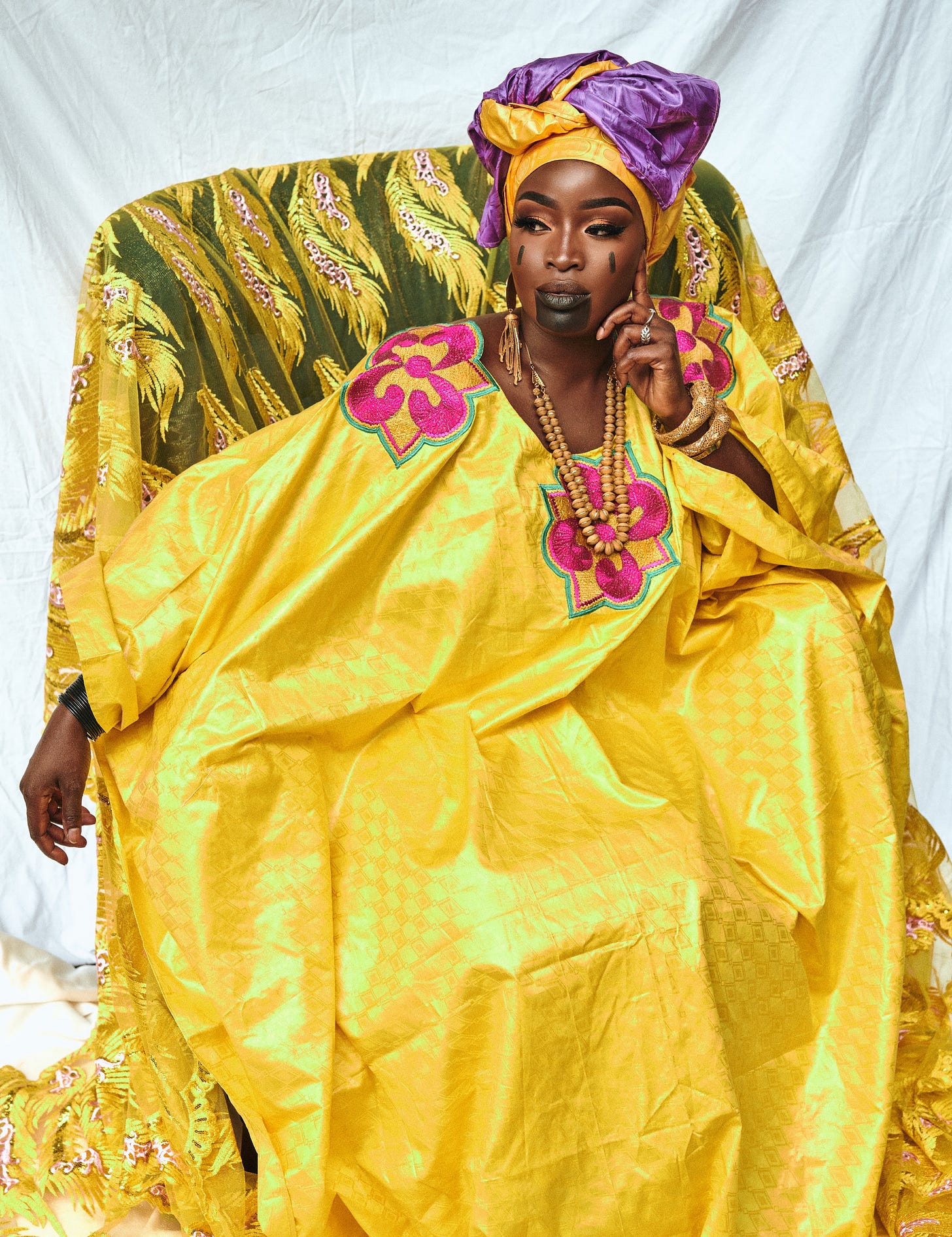 Lovette Jallow gazes sideways, wearing Fulani adornments, scarification, and layered goldenbeads. Lovette Jallow gazes sideways, wearing Fulani adornments, scarification, and layered goldenbeads.