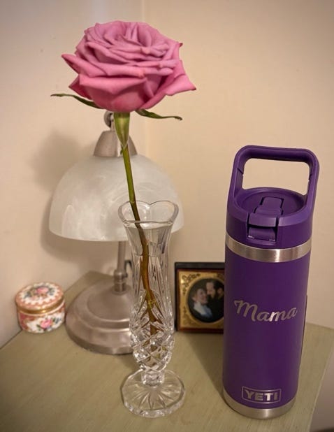 A rose in a vase next to a lamp and purple water bottle