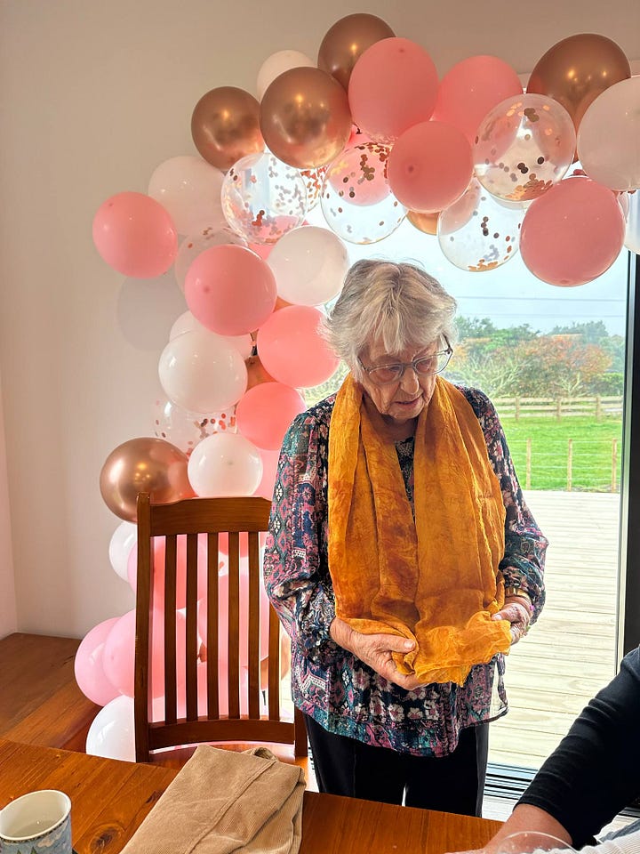 Both photos feature my nana. In the first photo with the whole family, her yellow orange scarf is the brightest pop of colour. In the second, the bright colour contrasts with the soft whites, warm gold and pink balloons behind her.