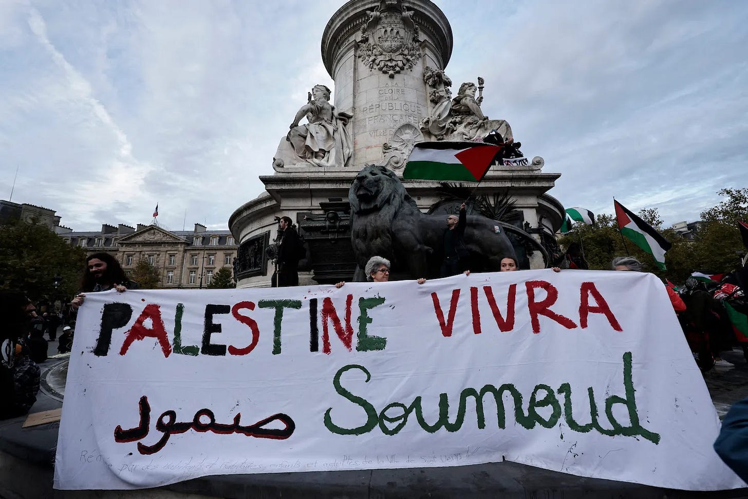 Participants hold a banner reading “Palestine will live” and wave a Palestinian flag during a demonstration in Paris.