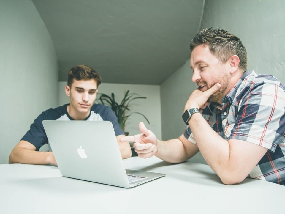 man wearing white and black plaid button-up sports shirt pointing the silver MacBook man wearing white and black plaid button-up sports shirt pointing the silver MacBook
