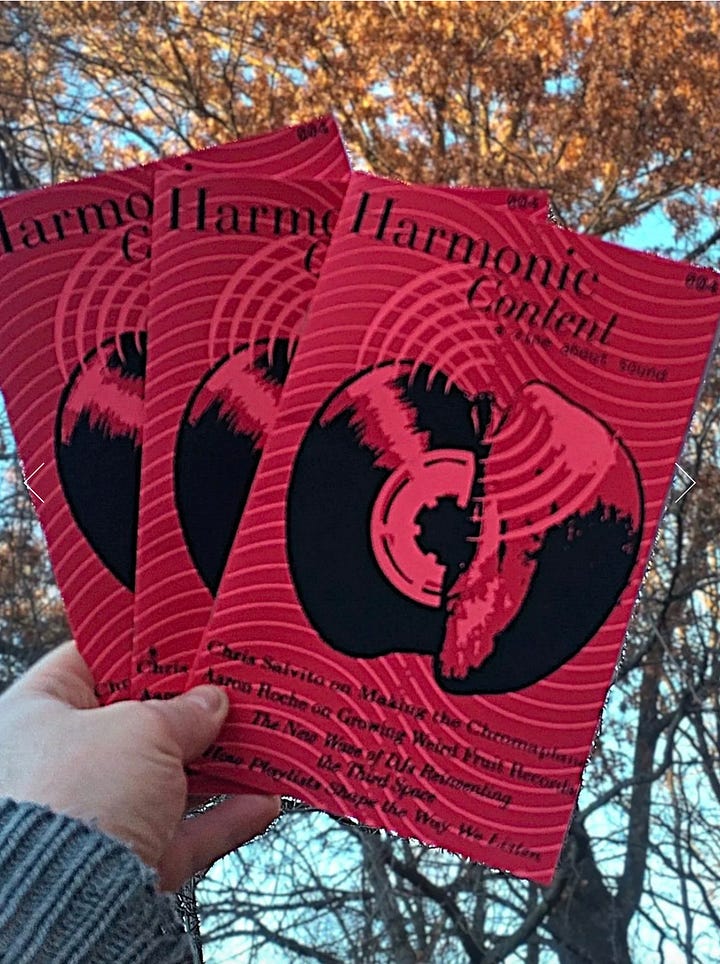 Harmonic Content zines photographed outdoors, held against autumn trees and resting on a wooden stringed instrument in grass.