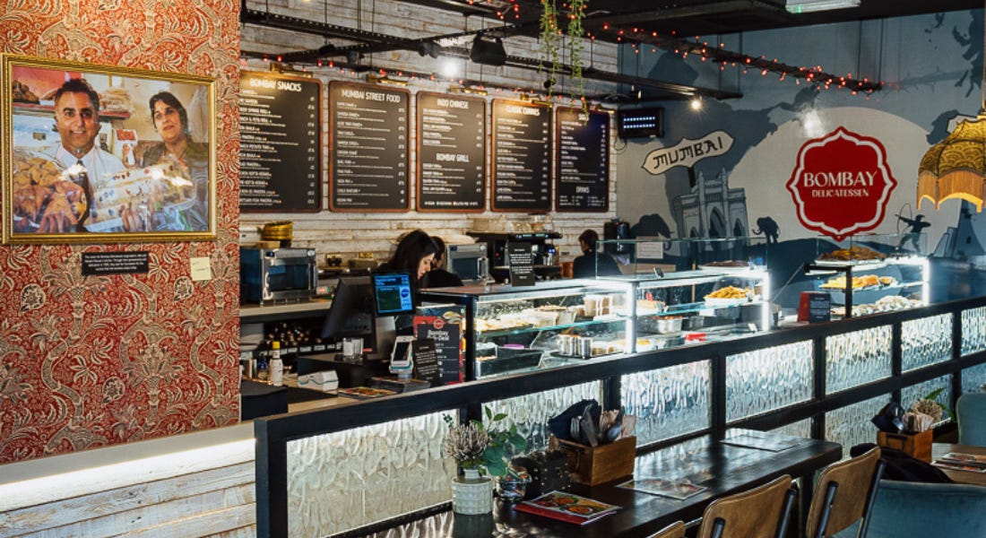 The inside of Bombay Deli with menus hanging on the wall, a picture of two people, and a dining area The inside of Bombay Deli with menus hanging on the wall, a picture of two people, and a dining area