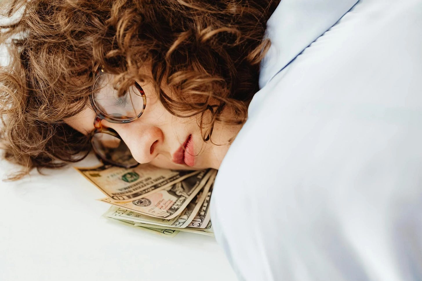 A white woman with curly hair and glasses sleeping on a pile of paper money