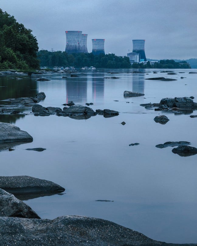 photo at dusk of river with rocks protruding and island in distance with 4 huge cooling towers with red lights photo at dusk of river with rocks protruding and island in distance with 4 huge cooling towers with red lights