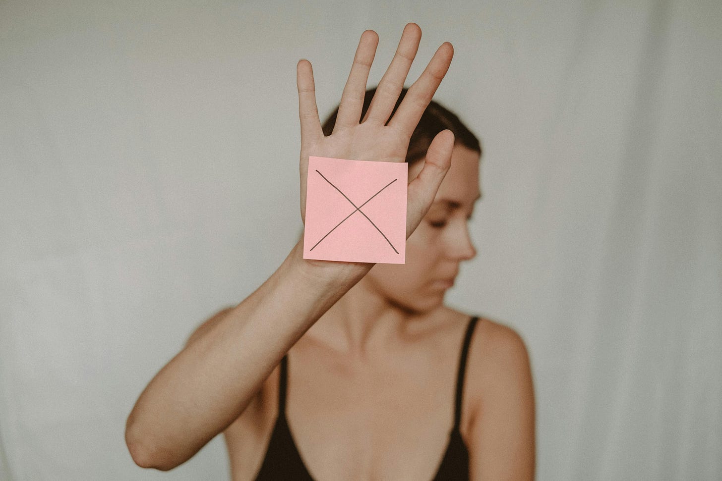 Woman holding up a sticky note with an X on it