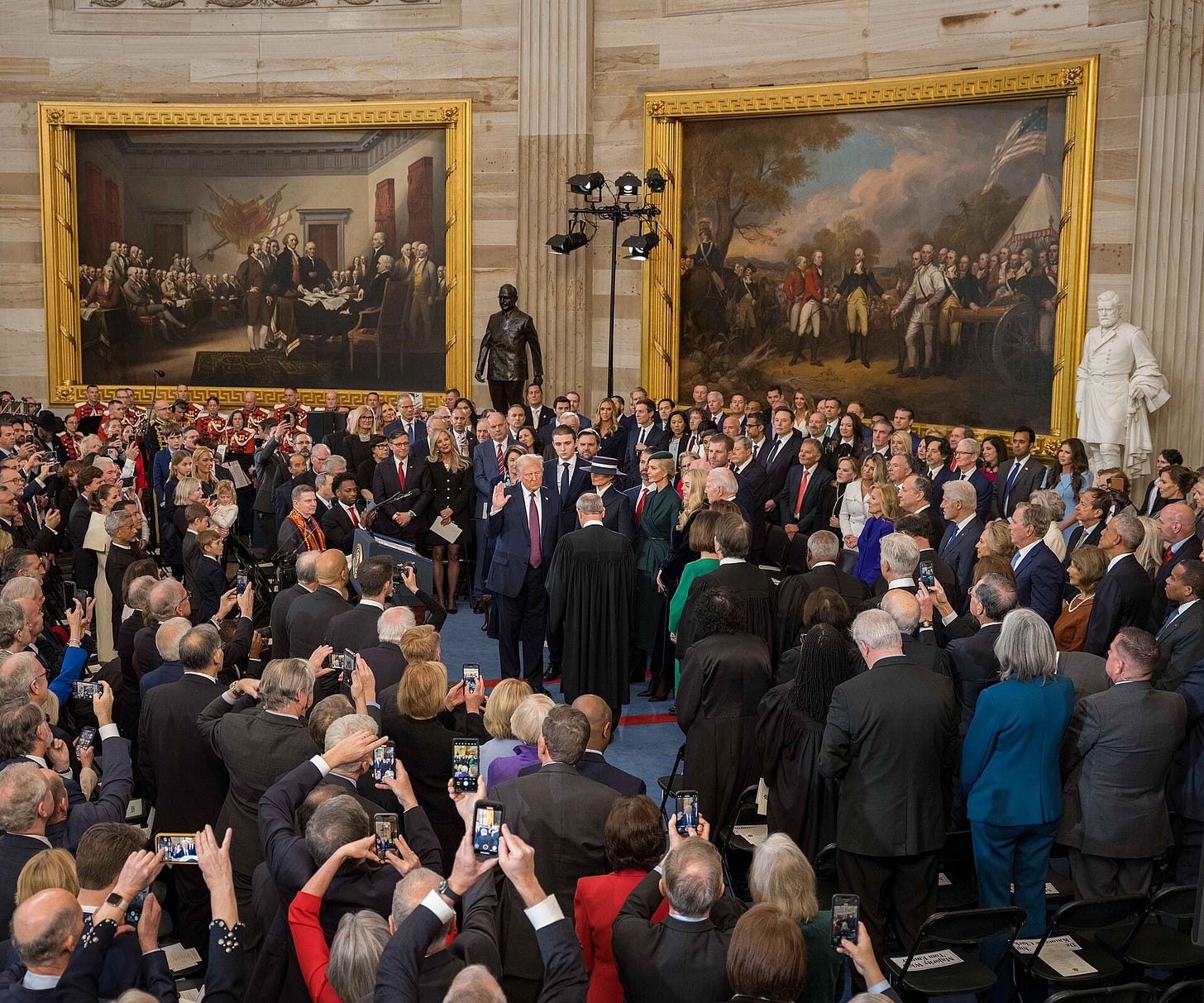 Donald Trump raises his right hand as he takes the oath of office indoors at the U.S. Capitol, with family members and officials standing around him.