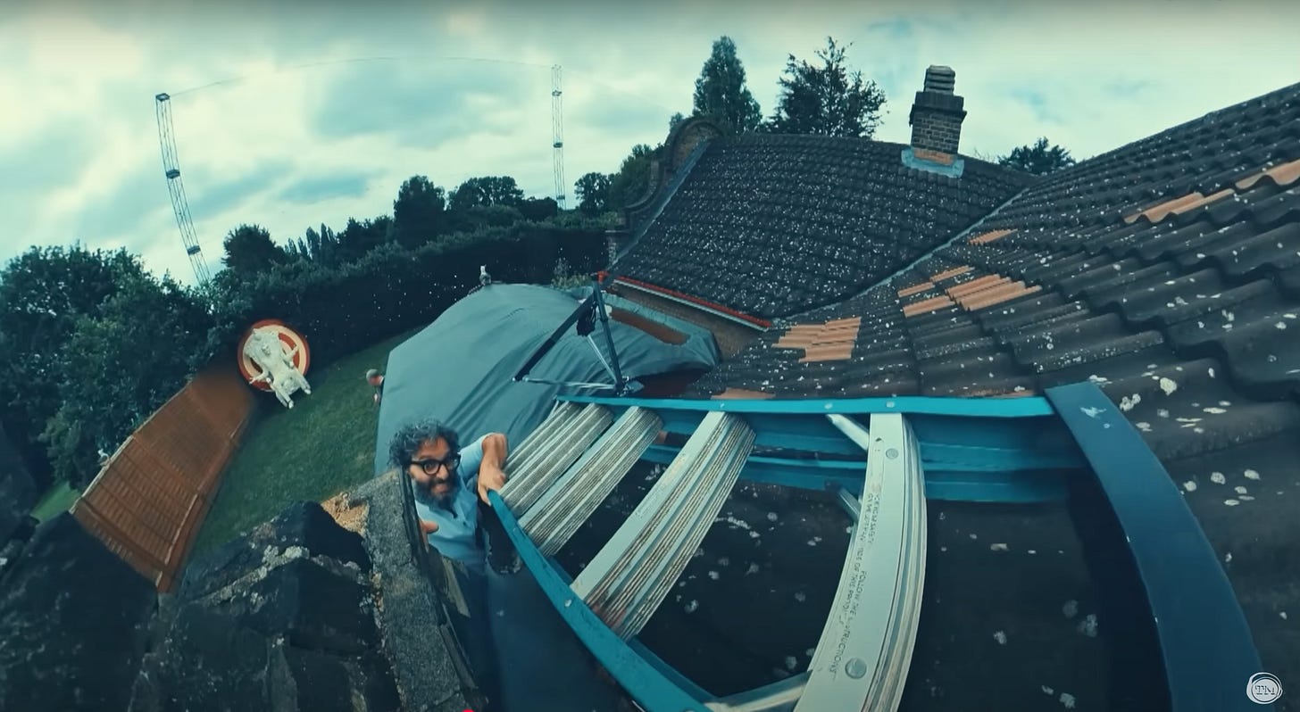 Jason Mantzoukas throws a ladder onto the roof of the Taskmaster house.