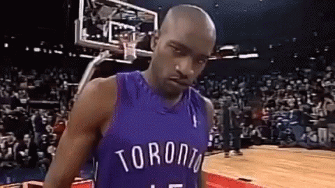 a man in a toronto raptors jersey is standing on a basketball court in front of a crowd .