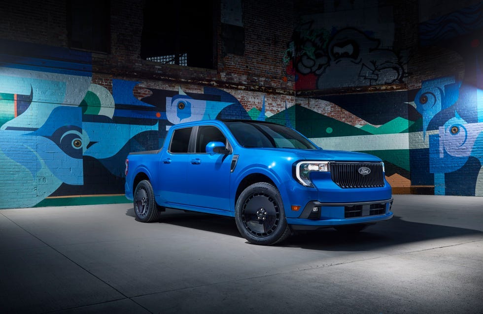 front three quarter view of a blue pickup truck parked in front of a colorful mural on a brick wall.