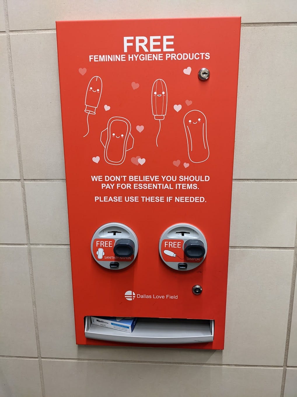 description: red machine on dallas airport bathroom wall with the words ‘free feminine hygiene products - we dont believe you should pay for essential items - please use these if needed.