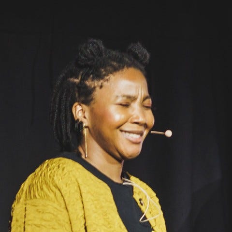 Catt smiling, eyes closed, speaking on stage with a headset microphone