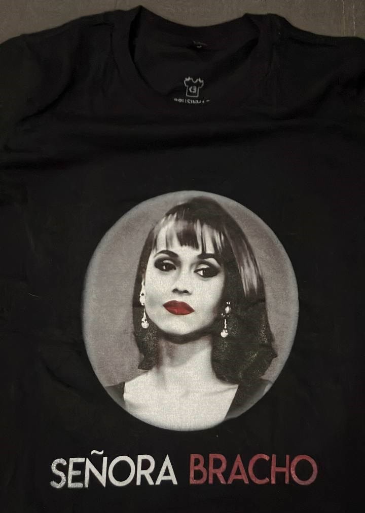 foto vista de cima de uma camiseta preta com uma estampa em preto, branco e vermelho. na parte superior é uma foto da paulina bracho olhando meio de lado, pra baixo, toda coqueta, com batom vermelho, brincos e o cabelo liso curto nos ombros. abaixo dela escrito em branco SEÑORA e BRACHO em vermelho. arte dramaturgia. foto vista de cima de uma camiseta preta com uma estampa em preto, branco e vermelho. na parte superior é uma foto da paulina bracho olhando meio de lado, pra baixo, toda coqueta, com batom vermelho, brincos e o cabelo liso curto nos ombros. abaixo dela escrito em branco SEÑORA e BRACHO em vermelho. arte dramaturgia.
