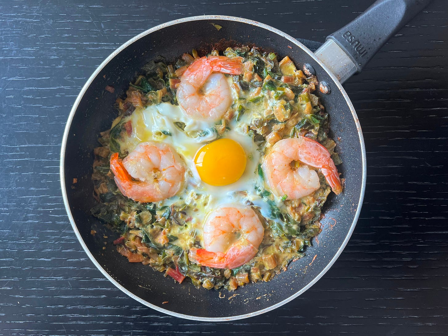 Mangold and spinach shakshuka with shrimp and eggs, served in a pan on a black surface. Part of Liat Portal’s Foodie Disorder journey on The Liat Show.