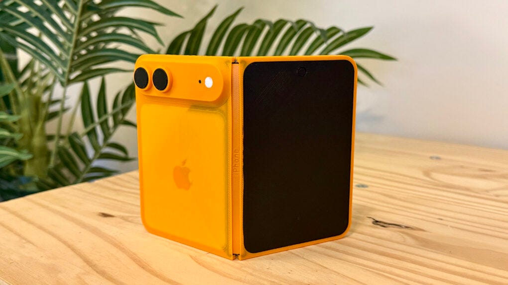 Orange folding iPhone model sitting on a pine table in front of a fake palm tree Orange folding iPhone model sitting on a pine table in front of a fake palm tree