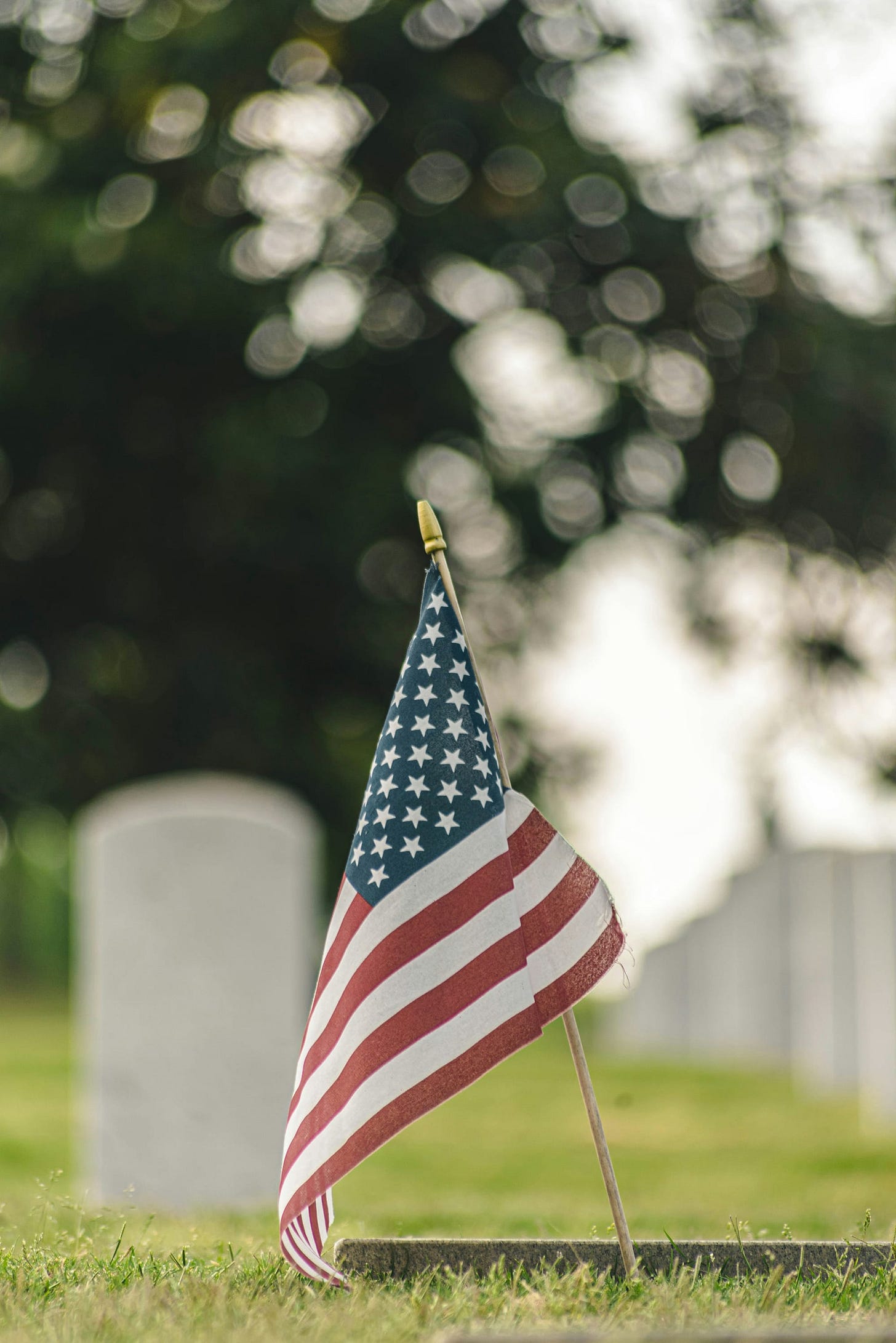 US flag posted in the grass, with tombstones in the background US flag posted in the grass, with tombstones in the background