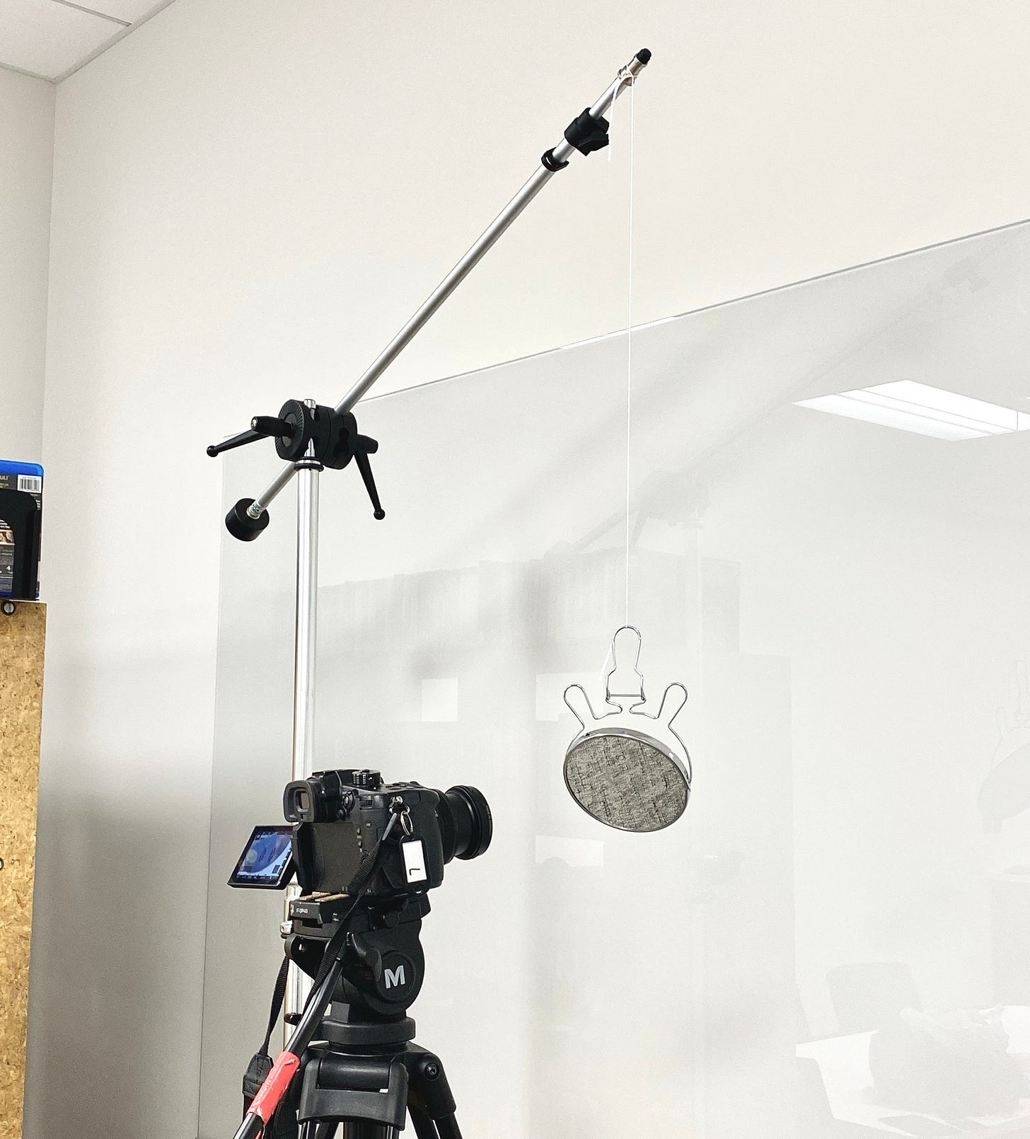 A DSLR camera is pointed at a round Dollar Tree makeup mirror hanging by a string from the arm of a c-stand in front of a white background.
