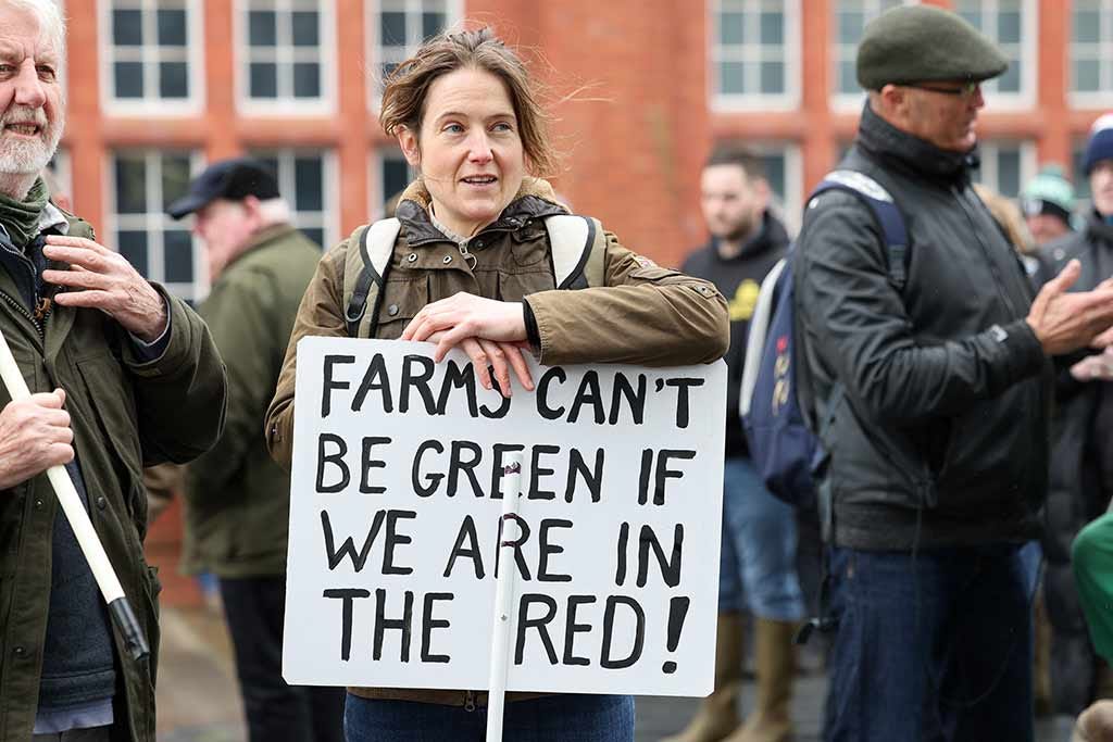 Farmers' protest placard held by a woman saying: Farms can't be green if we are in the red! Farmers' protest placard held by a woman saying: Farms can't be green if we are in the red!