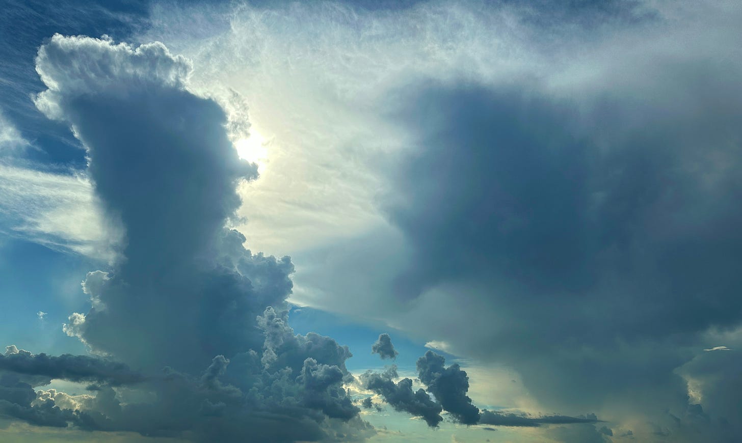 Storm clouds hang in an afternoon sky, the sun peeks