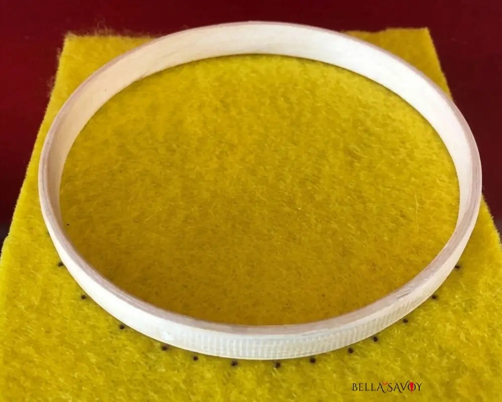 inner embroidery hoop sitting on yellow felt with black dots outlining the hoop