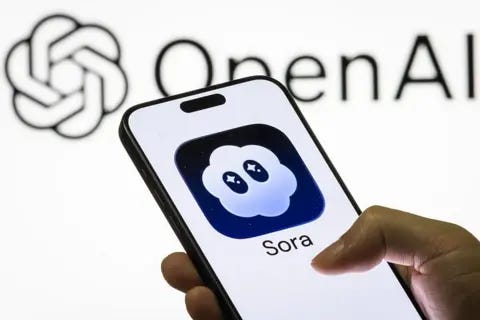 Getty Images A person holding a phone with the Sora logo. It is a cloud with eyes visible on the screen against a white backdrop with the OpenAI logo displayed.