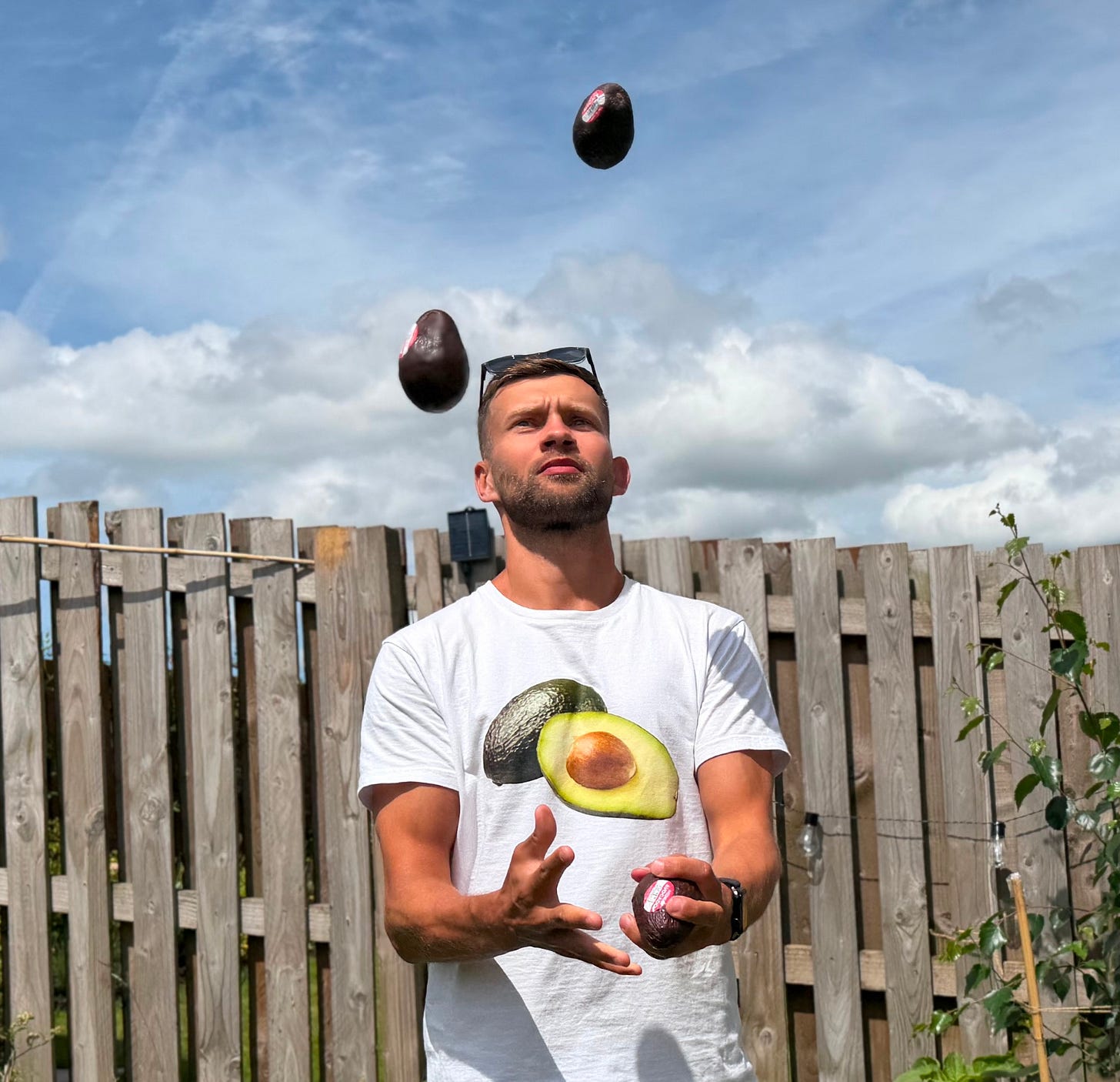 The author, Kuba, standing in a garden wearing an avocado T-shirt and juggling several avocados..