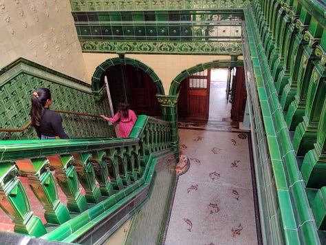 Metal turnstyle, pair of heavy wooden soors with stained glass windows, staircase with walls in tile