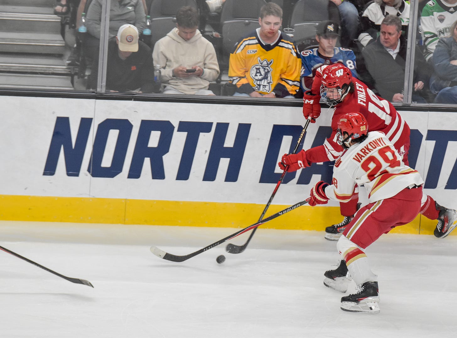 Quinn Finley along boards while trying to gain possession of puck with Denver player challenging for position.