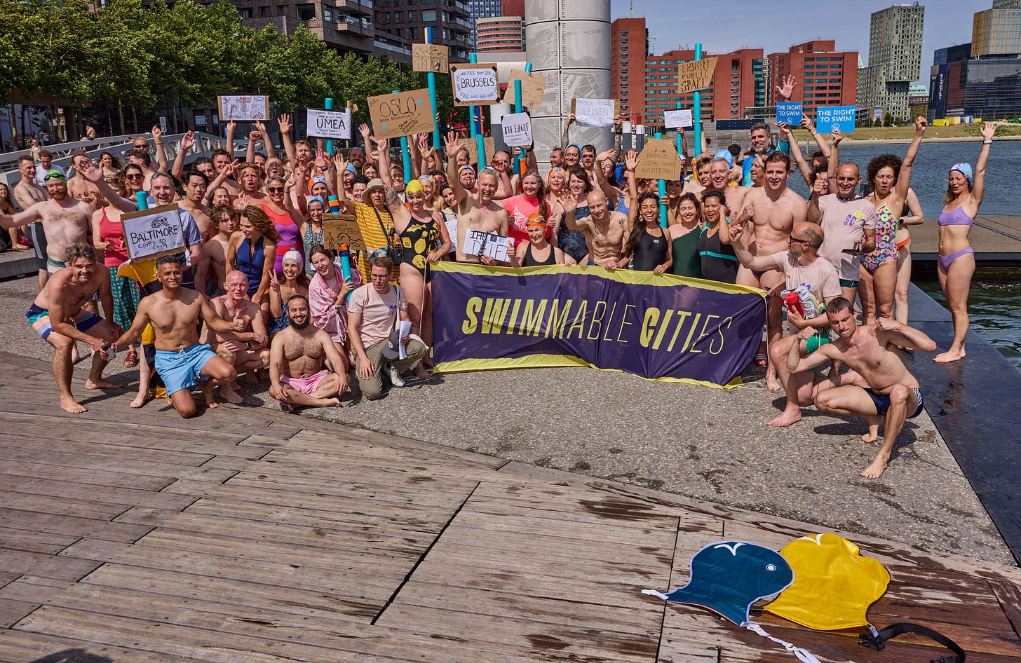 A group of about 50 people pose by an outdoor swimming, all in bathing suits