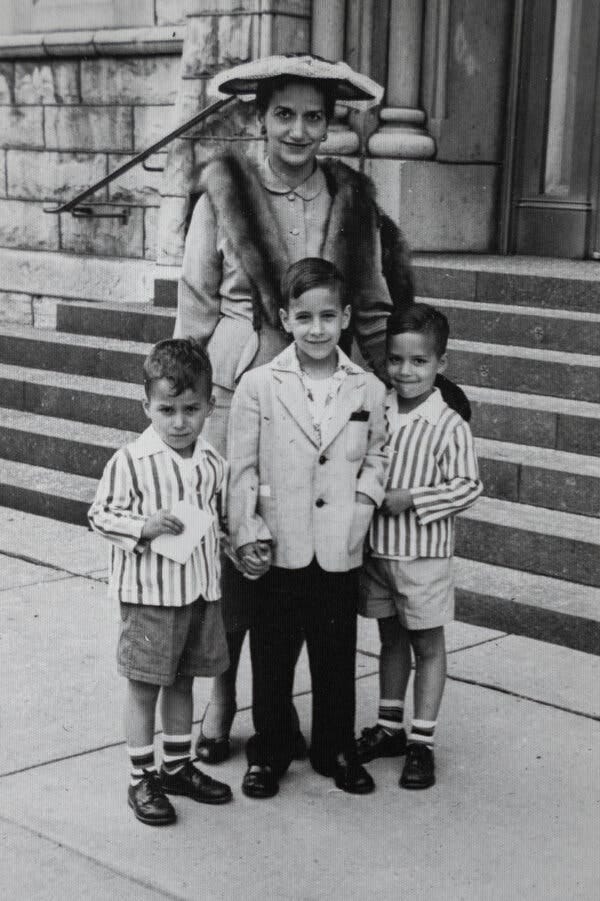 A woman in a hat stands behind three young boys.