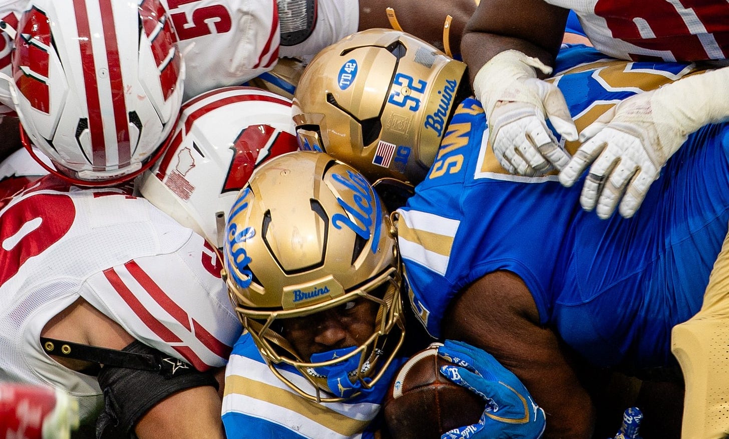 UCLA football player carries the ball into a group of Wisconsin defenders during a game at the Rose Bowl.
