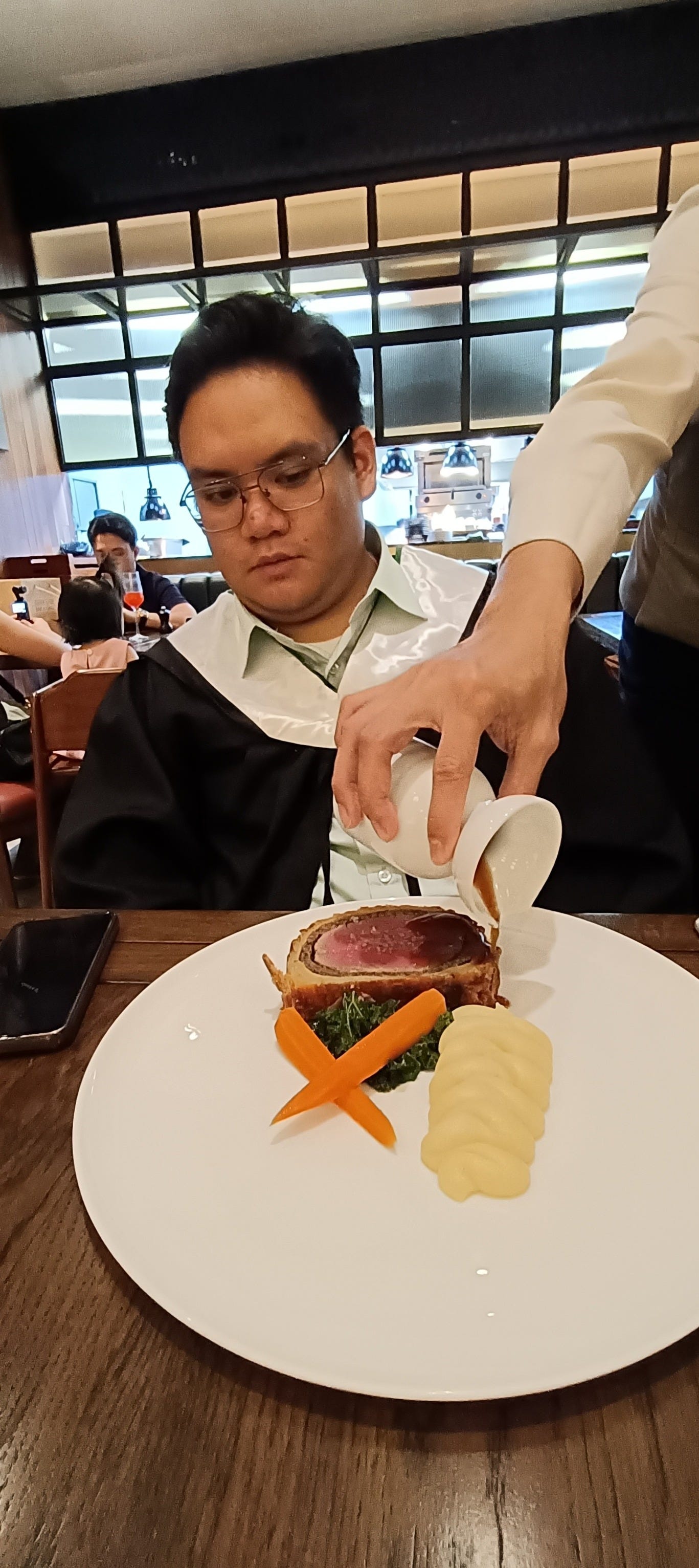 author's brother watching a server pour sauce over the beef wellington
