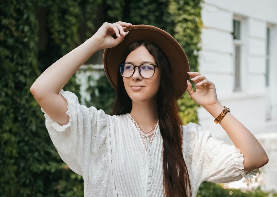 A woman wearing a hat and glasses standing in front of a house