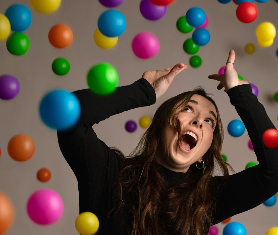 a woman in a black shirt and jeans is surrounded by balloons a woman in a black shirt and jeans is surrounded by balloons