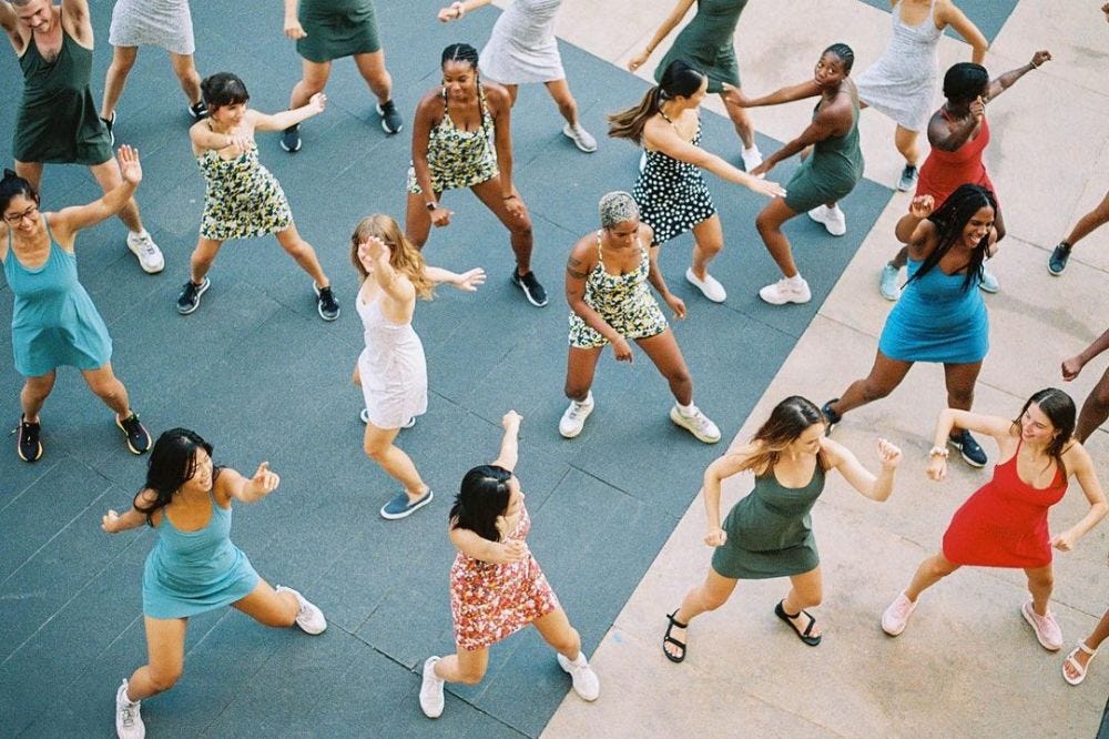 Women in colorful workout dresses dancing and jumping during an outdoor group fitness class Women in colorful workout dresses dancing and jumping during an outdoor group fitness class
