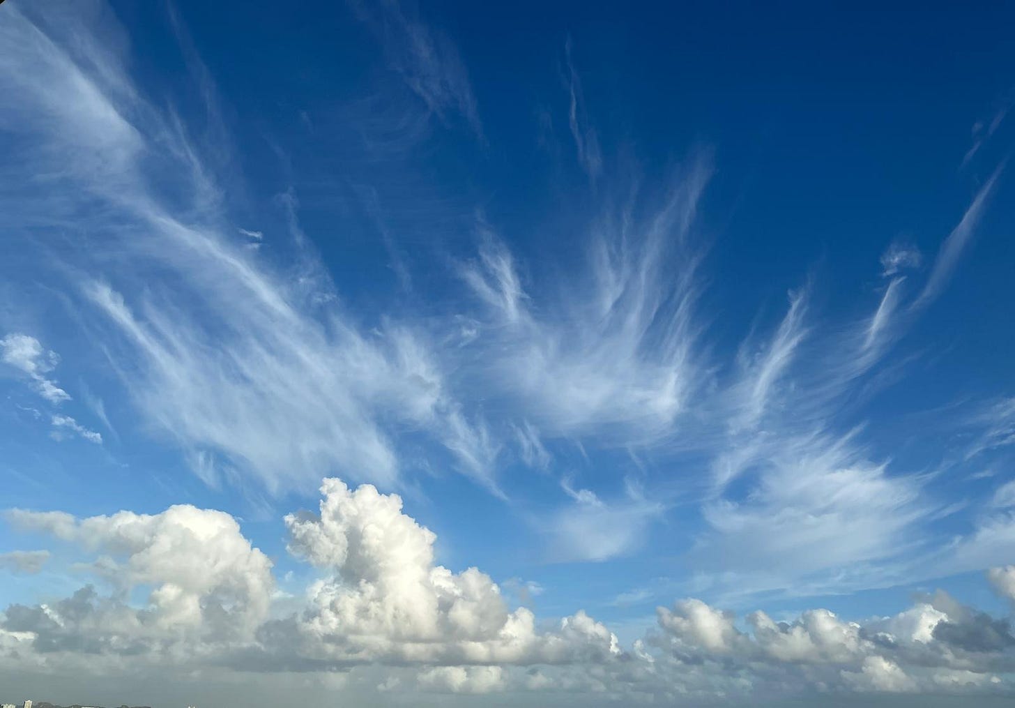 Wisps of white cirrus clouds pulling upward into a deep blue sky over soft, grounded clouds, symbolizing the soul's yearning to live forever.