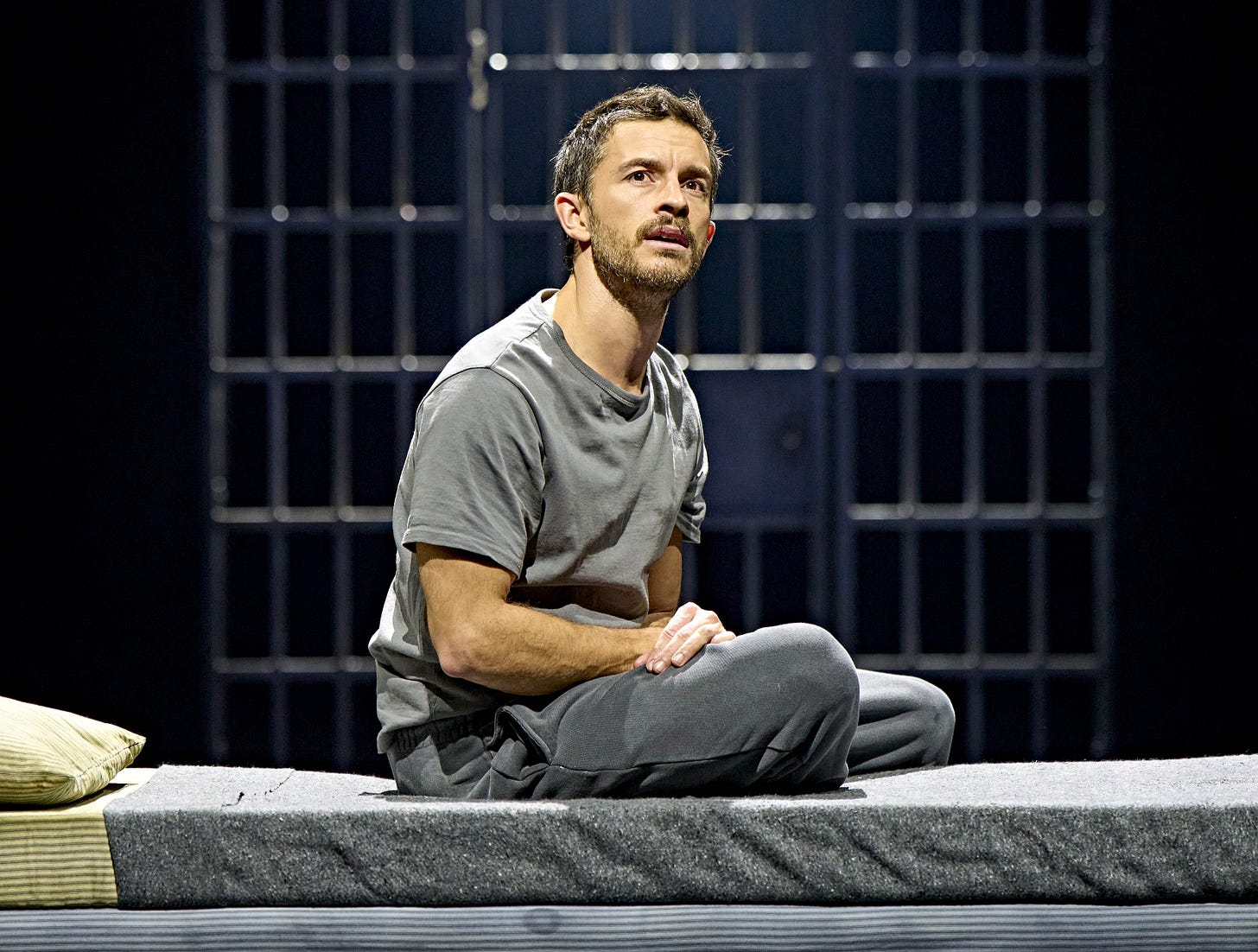 Jonathan Bailey in Richard II, dressed in jogging bottoms on a grey bed